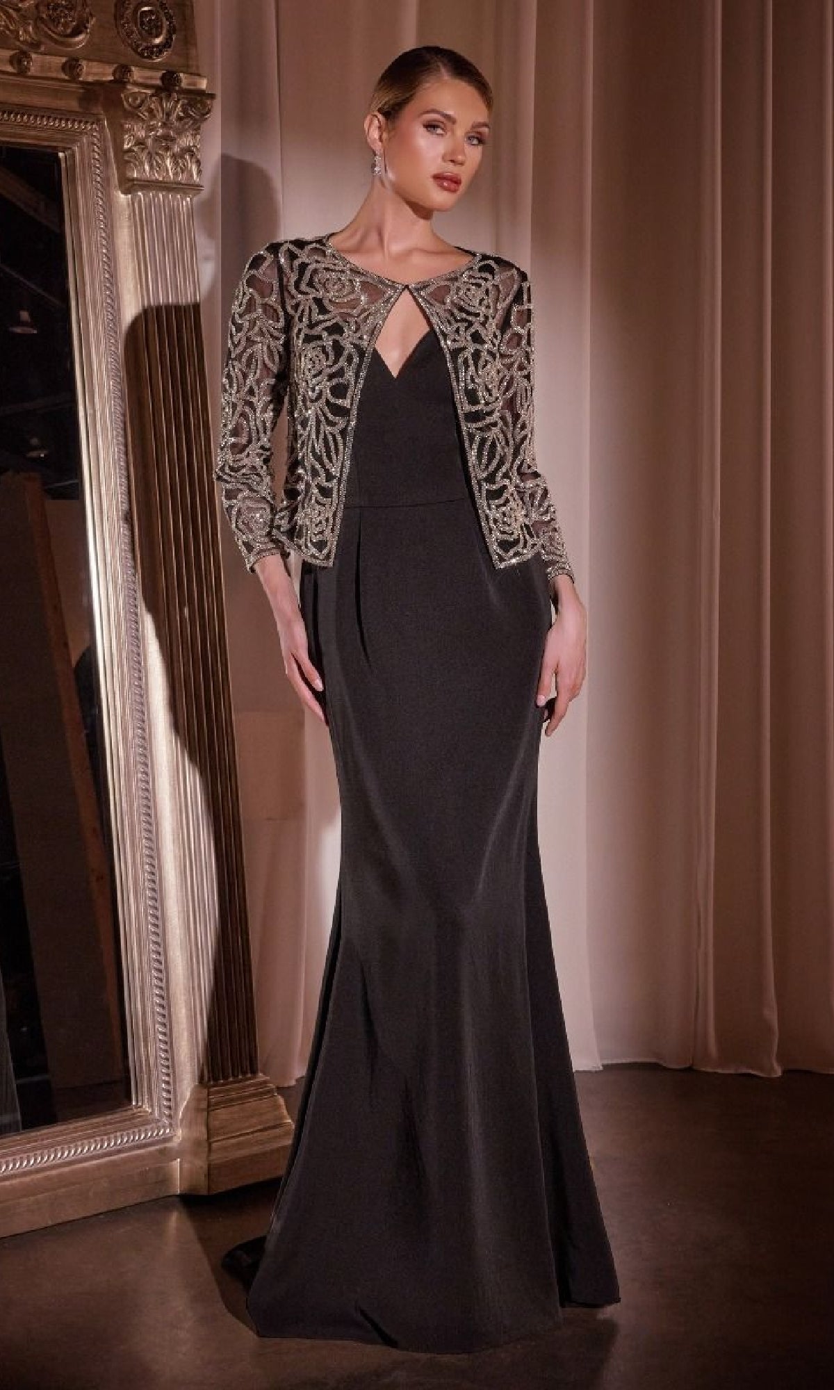 A woman stands indoors in the Ladivine J881 Beaded-Jacket Long Formal Dress, featuring a keyhole neckline and a fitted jacket with intricate silver embroidery—a sophisticated mother of the bride style.